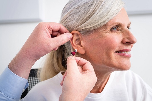 Eine Seniorin bekommt ein modernes Hörgerät von einem Hörakustiker ins Ohr eingesetzt.